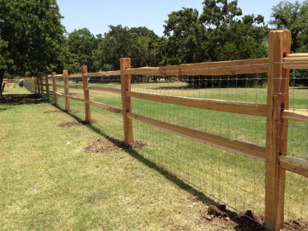 Cedar split-rail fence with wire mesh backing to contain livestock on rural property.
