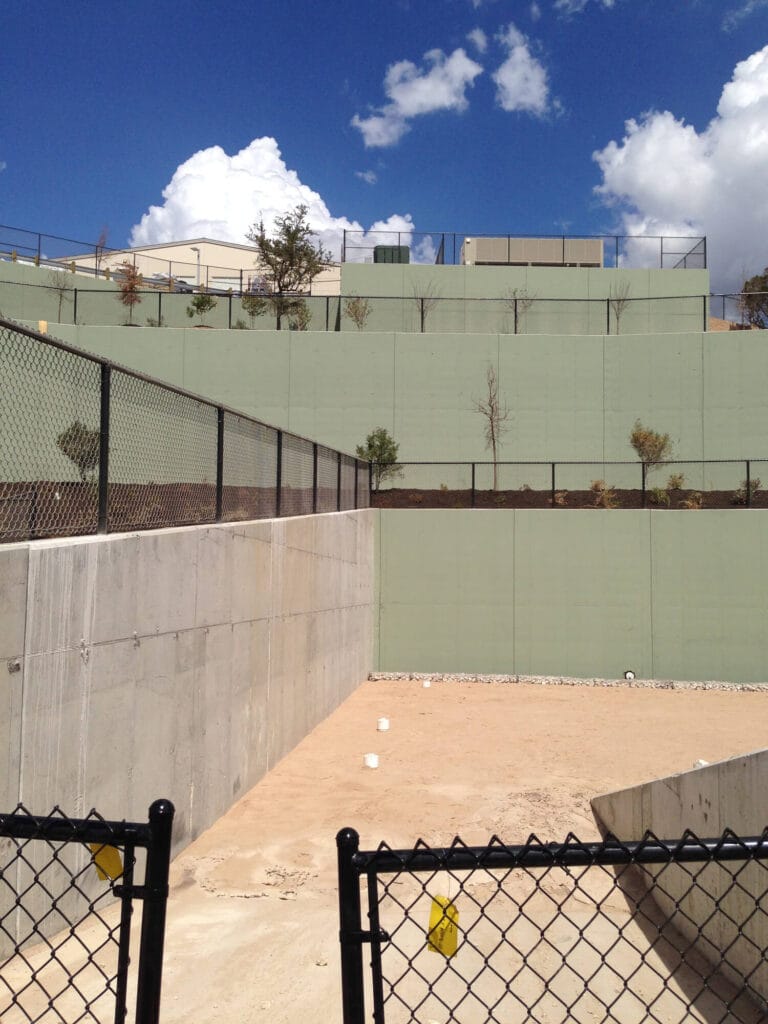 Black vinyl chain link fencing installed on uneven multi-tiered terrain for secure property boundary.