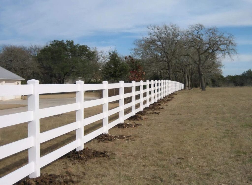 White vinyl four-rail perimeter fence outlining large property with clean, finished appearance.